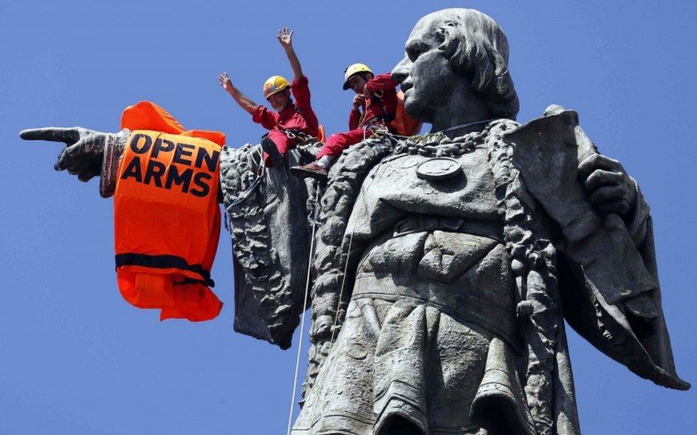 Activists place a lifejacket on the arm of the Columbus monument in Barcelona as the rescue vessel "Open Arms" arrives in the city