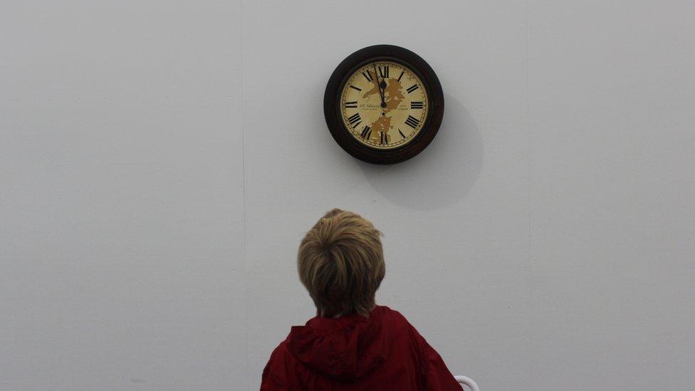 Bachgen ifanc yn edrych ar waith celf o gloc yn y Lle Celf // A child looking at an artwork of a clock in a gallery