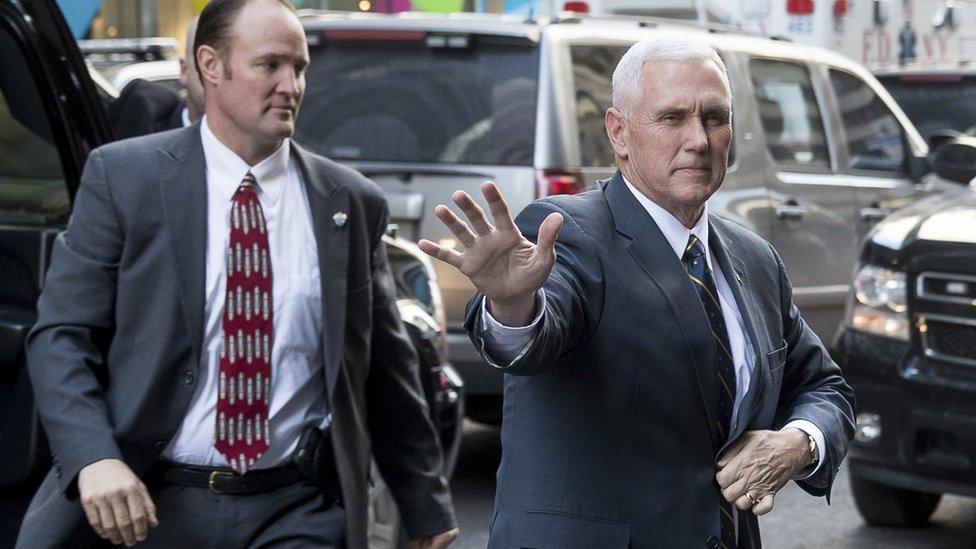 Mike Pence, right, hold one arm outstretched in a wave as he crosses the road to enter Trump Tower in New York, flanked by men in suits