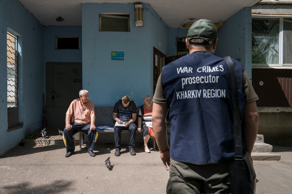 A Kharkiv police officer interviews residents of a block of flats that was shelled, while a prosecutor looks on. The testimony could become evidence in a war crimes tribunal.