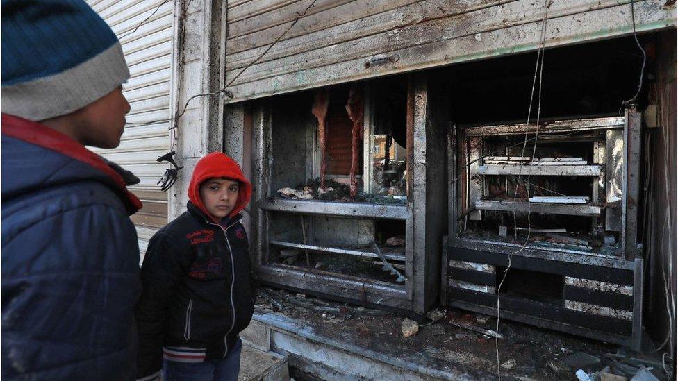 Syrian boys look at the destroyed grills outside a shuttered-down restaurant which was the site of a suicide attack targeting US-led coalition forces in the flashpoint northern Syrian city of Manbij