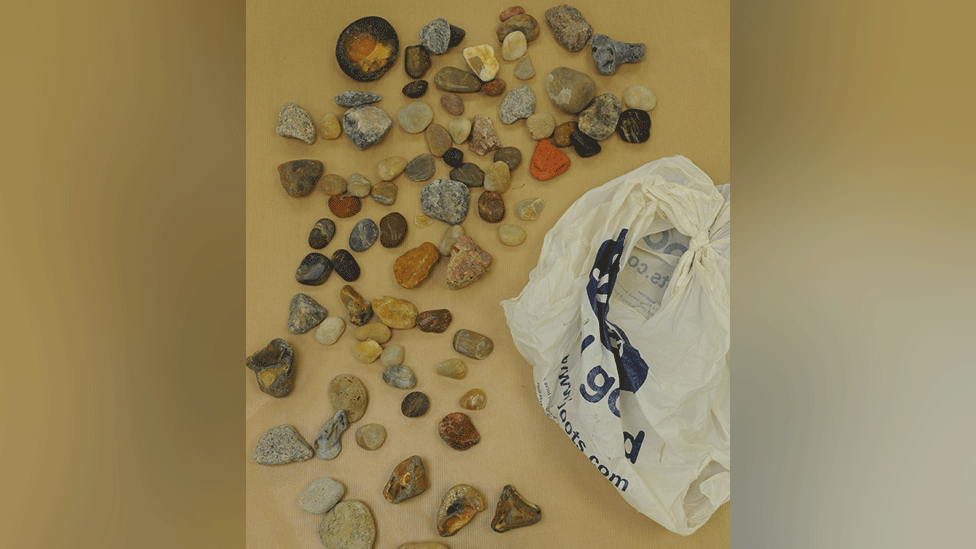 Decorative stones and pebbles laid out on a table next to a white Boots carrier bag