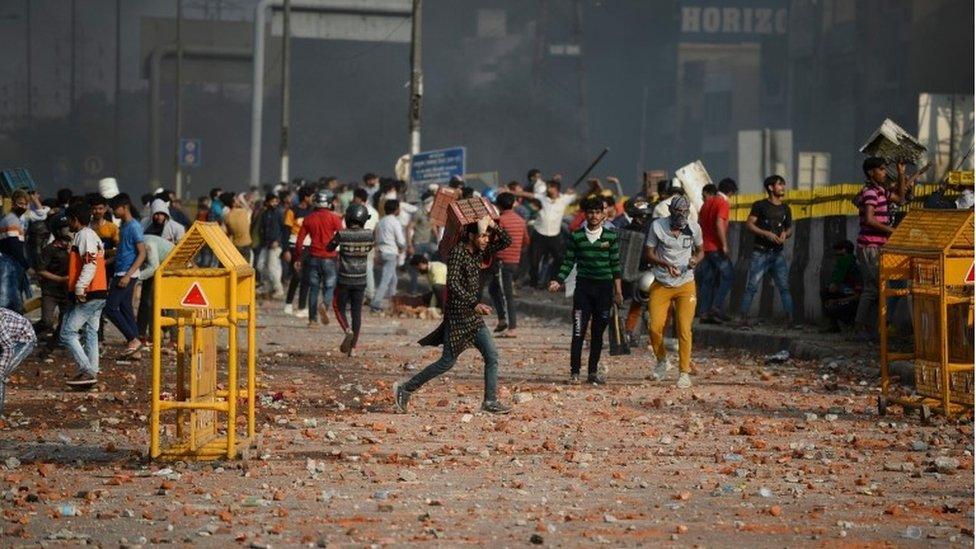 Demonstrators gather along a road scattered with stones following clashes between supporters and opponents of a new citizenship law, at Bhajanpura area of New Delhi on February 24, 2020