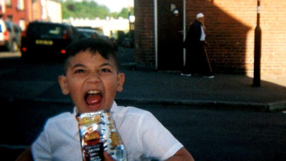 Young boy with bag of crisps, old man in background