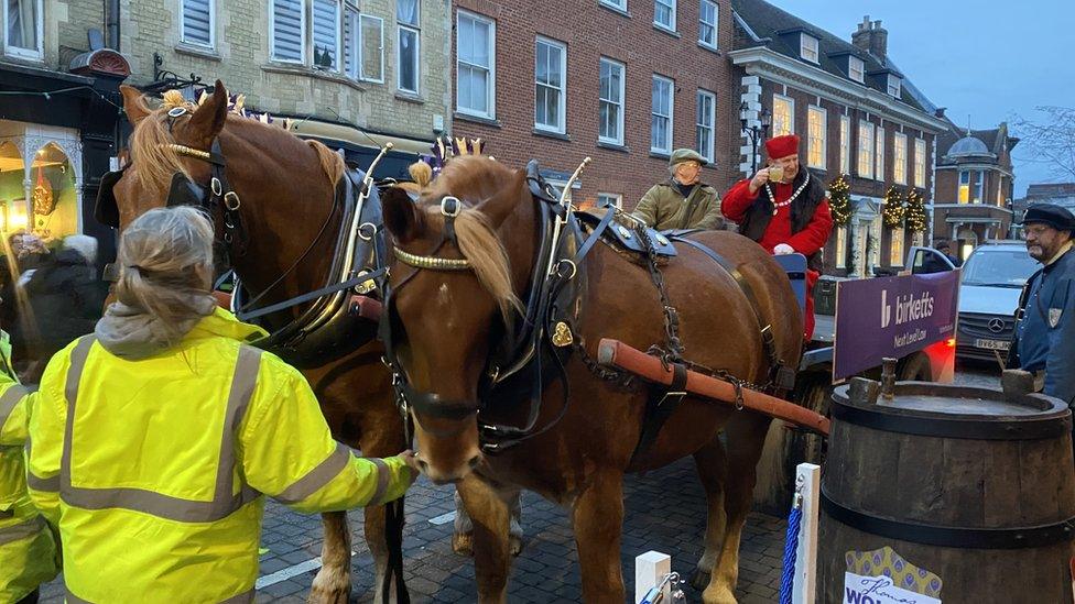 Two large brown horses pulling a cart on which a man in Tudor dress is sitting