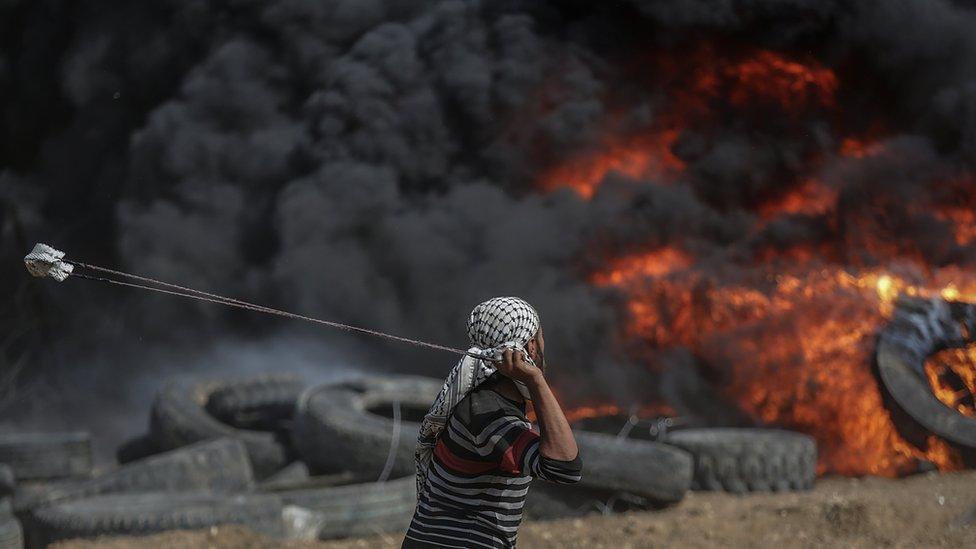 A Palestinian hurls a stone towards Israeli troops during a protest on the Gaza-Israel border on 27 April 2018