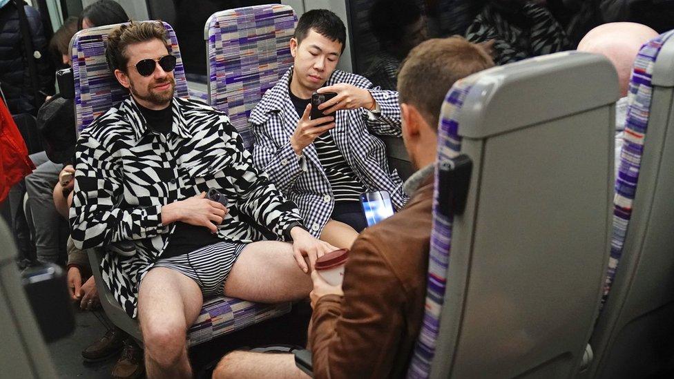 A group of men sat facing each other wearing black and white patterned outfits and stripy underwear.