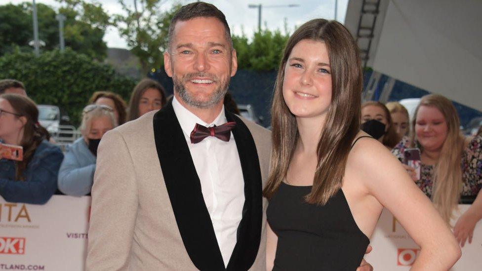 Fred Sirieix and Andrea Spendolini-Sirieix attend the National Television Awards 2021 in London. Fred has short greying brown hair, blue eyes and a short beard. He wears a camel-coloured tux with brown lapels matched with a white shirt and burgundy bow tie. Andrea wears a black dress and her long brown hair is worn loose.