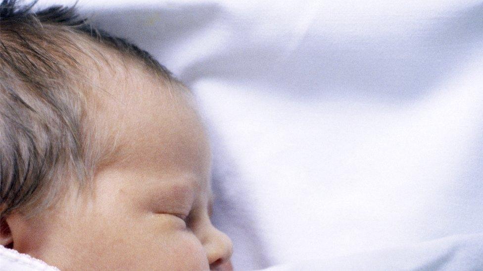 A baby asleep under a blanket in a cot