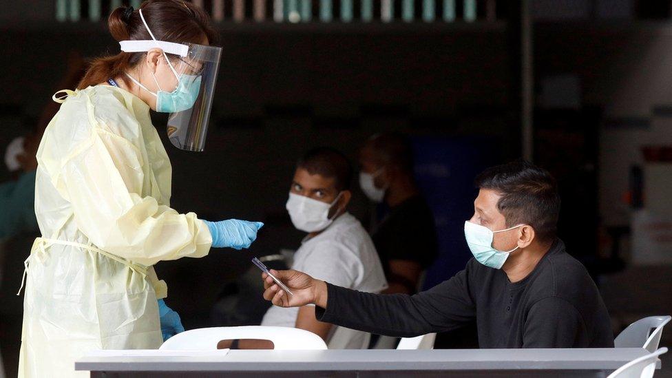 A medical professional talks to migrant workers as they wait to be transported to a medical facility from their dormitory