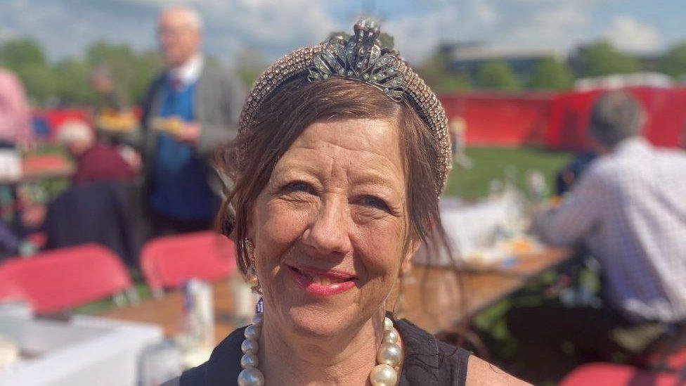 Frances Morris sitting down. She has black hair and is wearing a glittering head band and large pearl necklace.