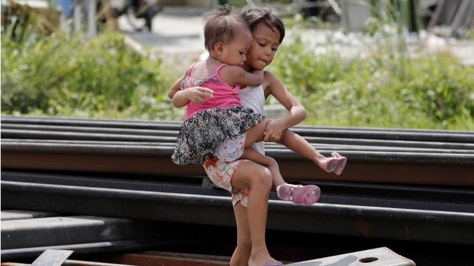 A Filipino girl carrying a baby maneuver amongst metal barriers at a river dike project ahead of an impending super typhoon