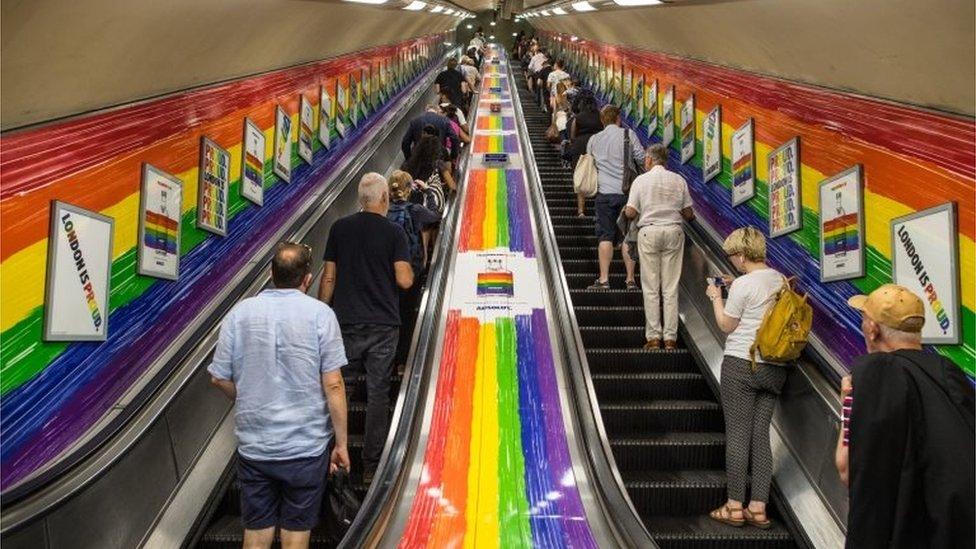 People ride a tube escalator decorated with the Pride flag colours