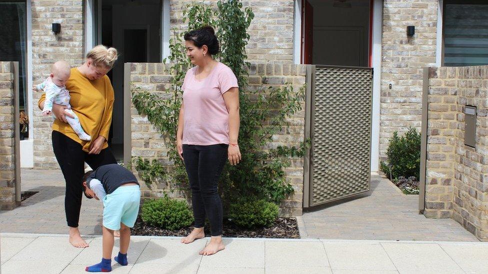 Two mothers and their children stand outside their houses