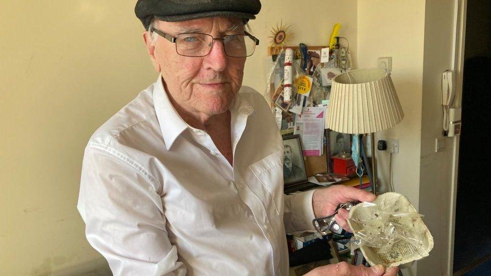 Man in flat cap holds Sellotape onto which are stuck several small black bugs.