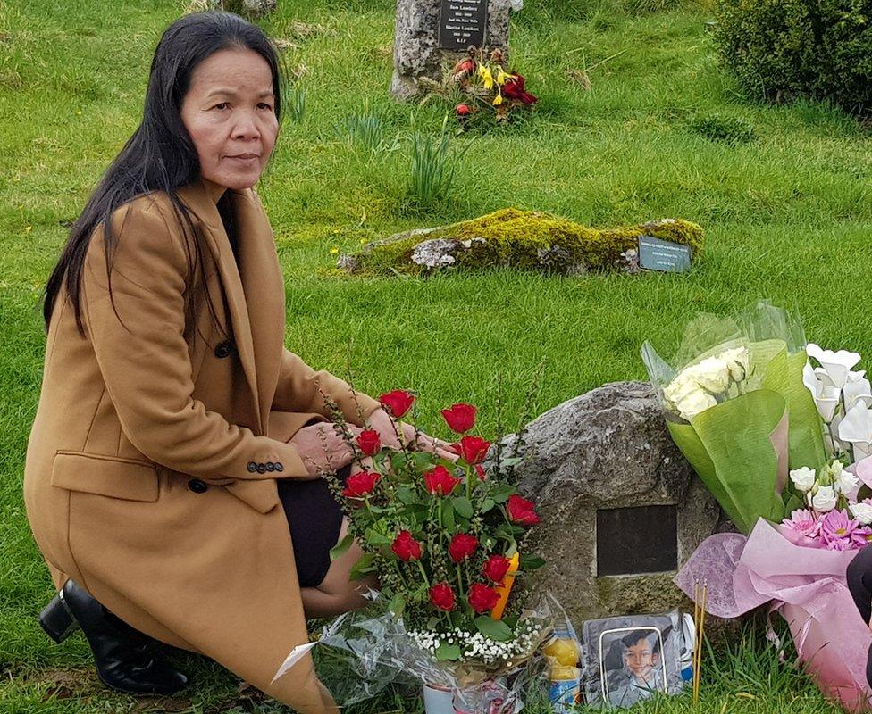 Thai woman kneeling at a graveside, which is surrounded by flowers