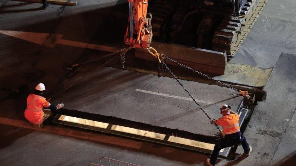 Council workers seal the artist beneath the road with heavy equipment