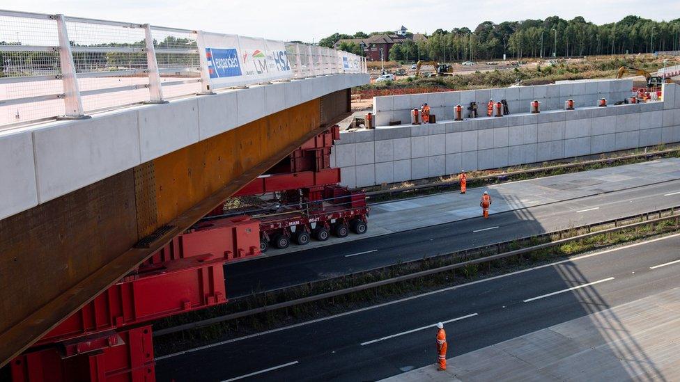 HS2 workers watch as a bridge is wheeled into position over the M42