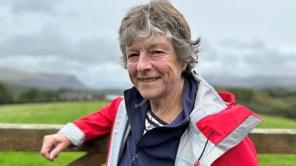 A woman in a red mountain rescue jacket smiles at the camera