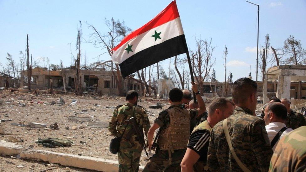 Forces loyal to President Assad walk through Aleppo as one of them holds up a Syrian national flag