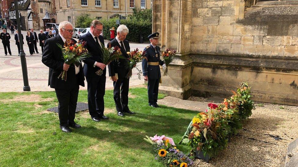 Cllr Alan Preest, Chair of Gloucesterhire County Council, Cllr Mark Hawthorne, leader of GCC, Edward Gillespie, Lord Lieutenant and Sir Dusty Miller, High Sheriff of Gloucestershire lay what would have been the winners flowers from the Tour of Britain outside Gliucester cathedral in memory HRH The Queen.