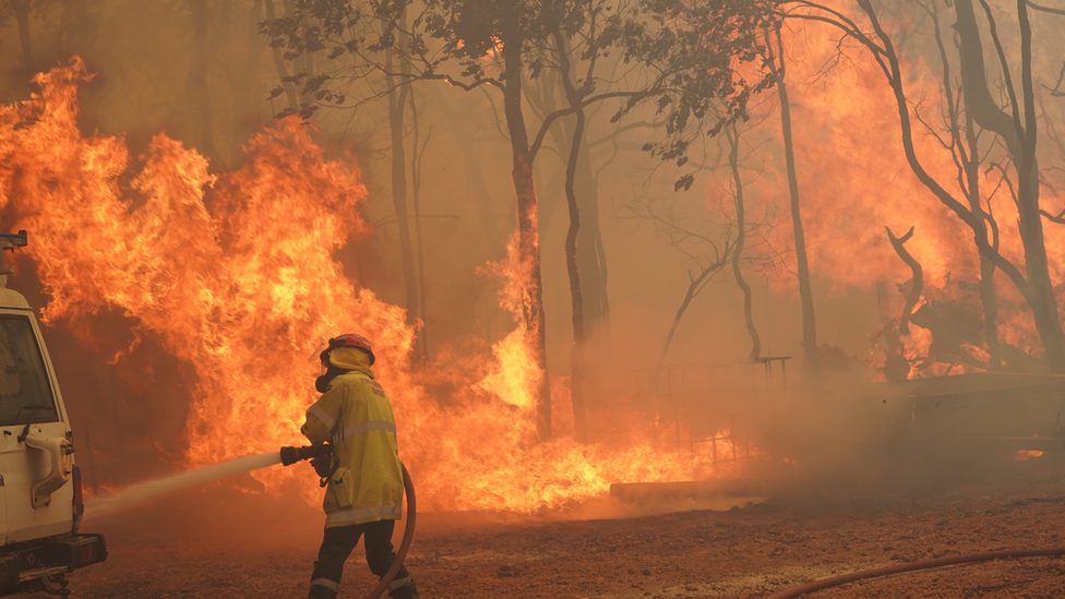 Firefighter hoses down a vehicle in front a fire in Brigadoon