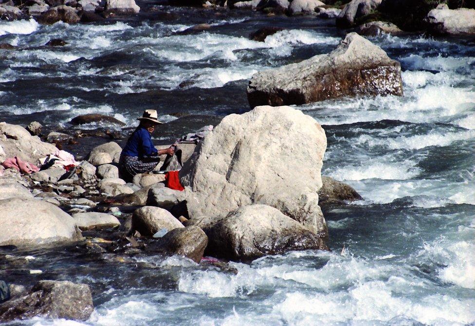 A woman washes her clothes in a fast running stream