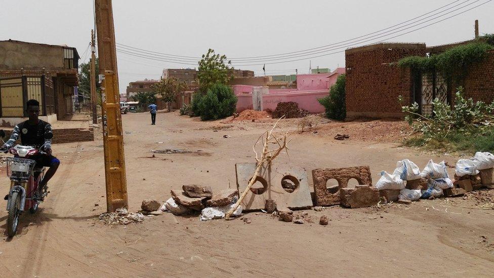 A man on a bike navigates around a makeshift roadblock made up of sticks and blocks of concrete