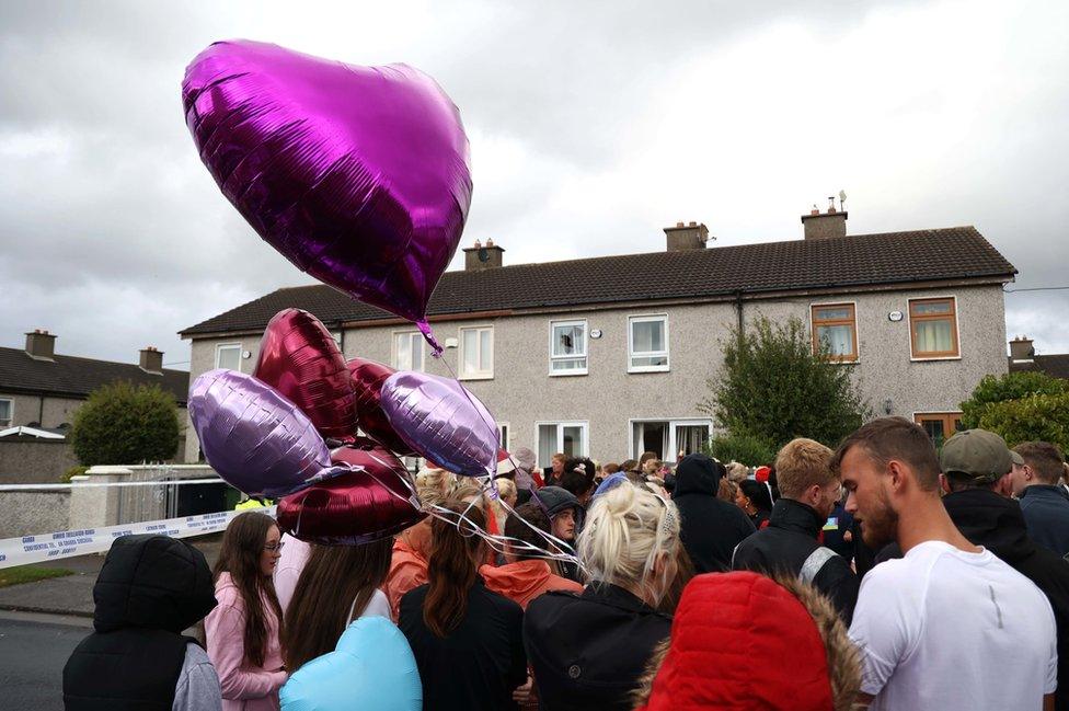 People hold pink heart-shaped balloons at the vigil for Chelsea and Christy Cawley and Lisa Cash outside their home in Tallaght in Dublin