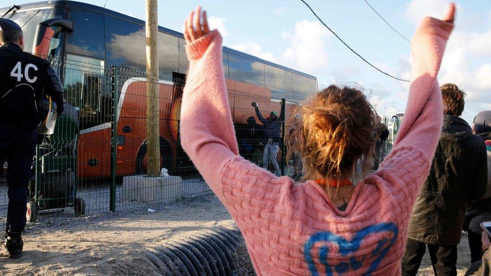 a volunteer waves to departing migrant minors