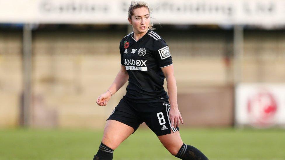 Maddy Cusack playing football, she's running on the pitch and wearing a black and white kit