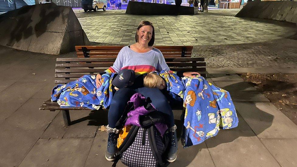 A woman with sons asleep on a bench in London