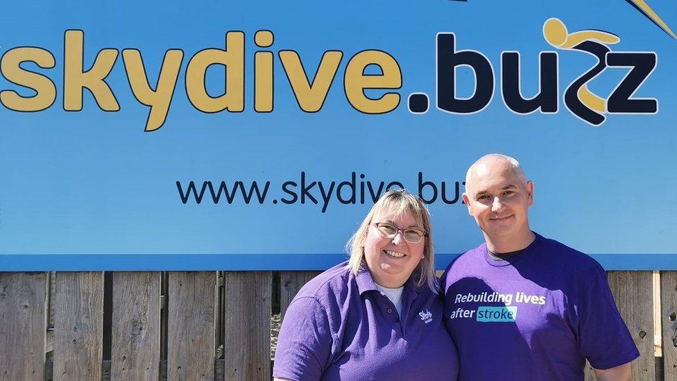 Sarah Luxton and her brother Wayne Ewing standing in front of a skydive banner with purple shirts on that say 'rebuilding lives after stroke'