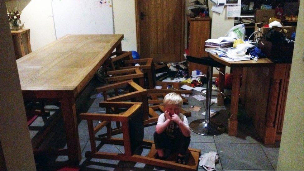 Jamie in the dining room, surrounded by chairs and objects pushed to the floor