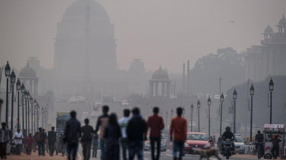 Indian pedestrians walk near smog enveloped government offices on Rajpath in New Delhi on December 1, 2015.