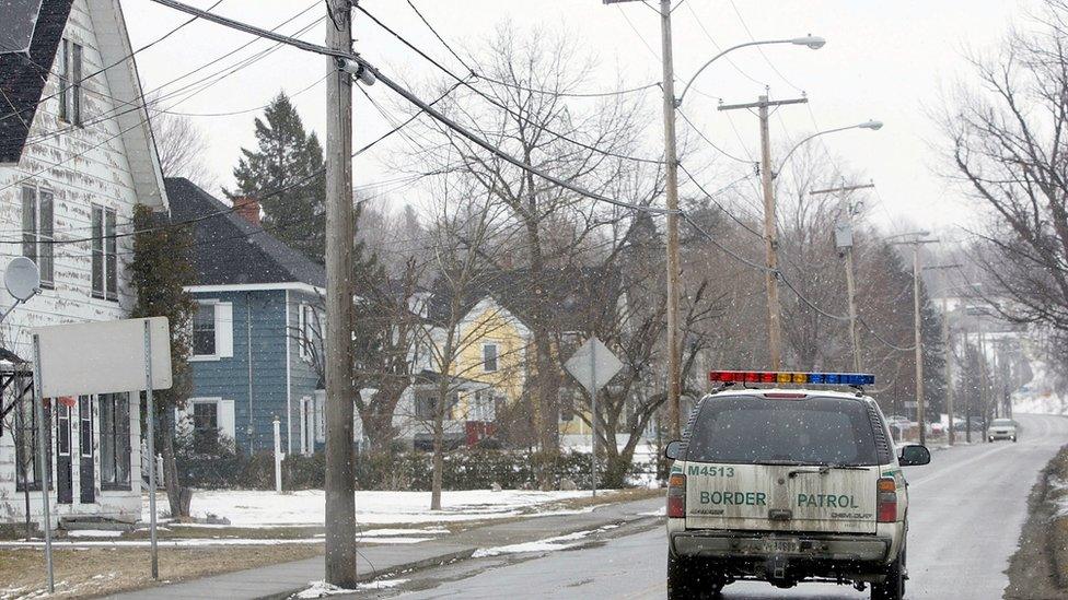 A US Border Patrol Agent drives his vehicle on the US side of a two lane road that separates Canadian territory from the US