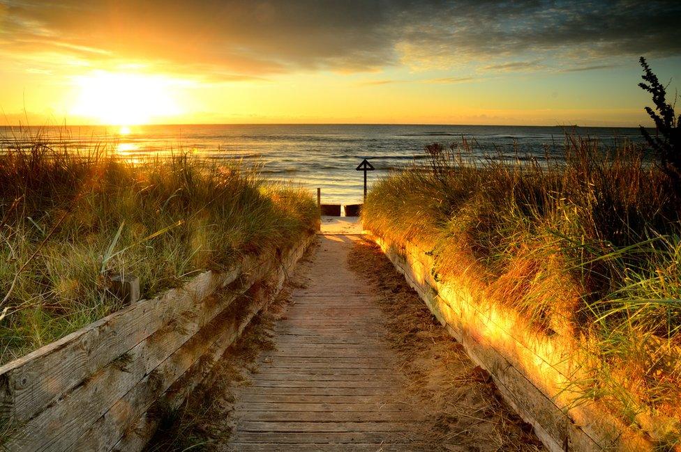 View down path to beach with sun rising over sea