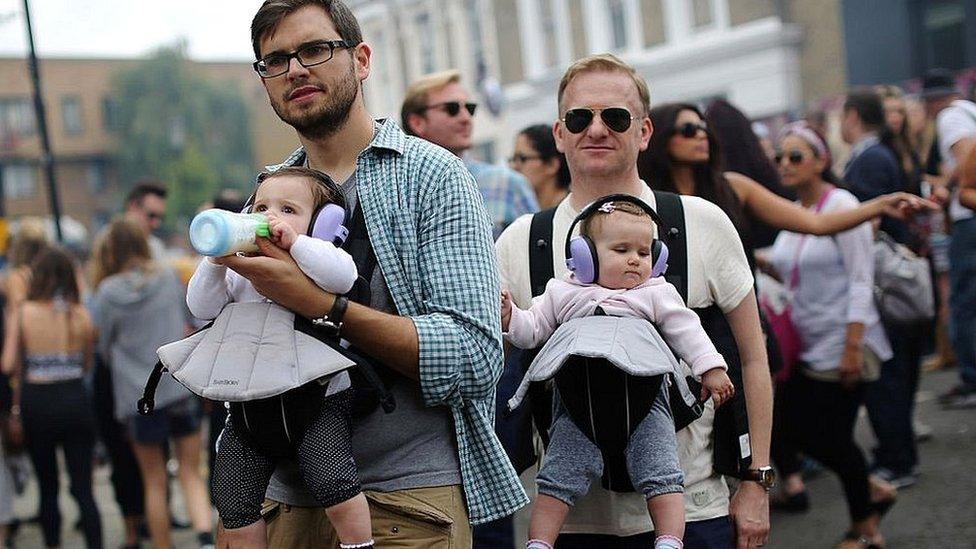 Two men carry children wearing ear protection during the Notting Hill Carnival 2014