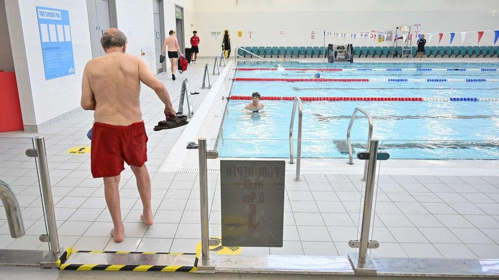 Swimmers carry their outdoor clothing and shoes out of the pool area after swimming at Kensington Leisure Centre in west London on July 25, 2020 as novel coronavirus lockdown restrictions are eased to allow gyms, leisure centres and indoor swimming pools in England to reopen. - England's gyms, leisure centres and indoor swimming pools were allowed to open their doors on July 25 for the first time since the March