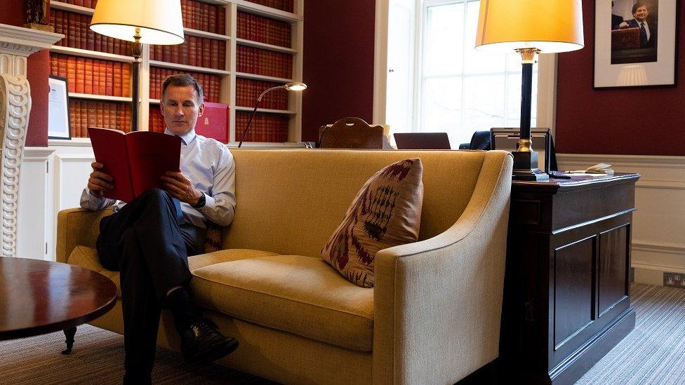 Chancellor Jeremy Hunt sits on a sofa reading through a copy of the upcoming Budget