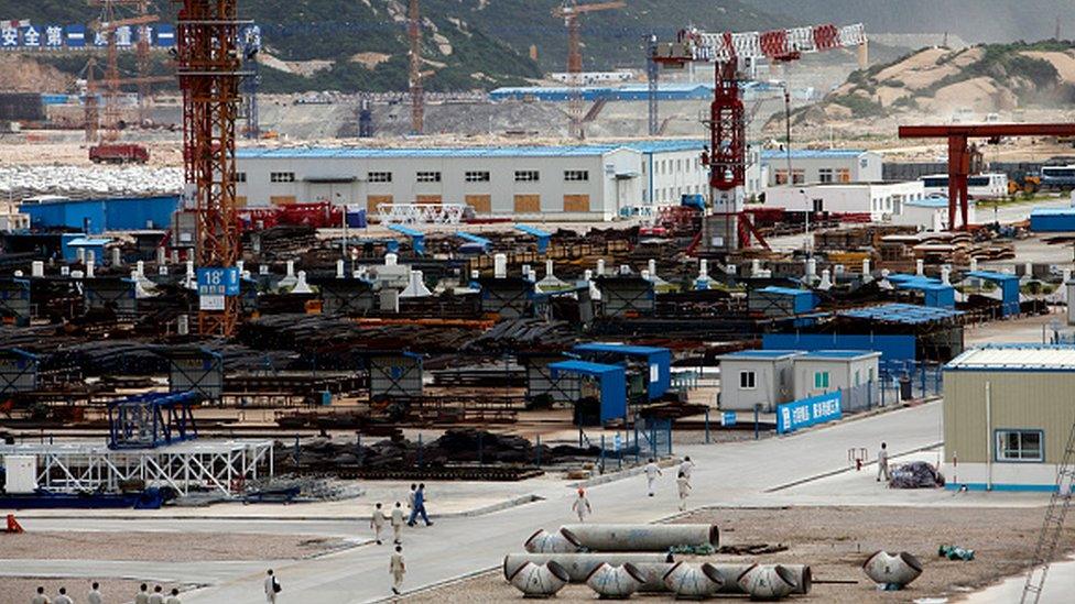 Workers walk through the material supply yard at the Taishan plant