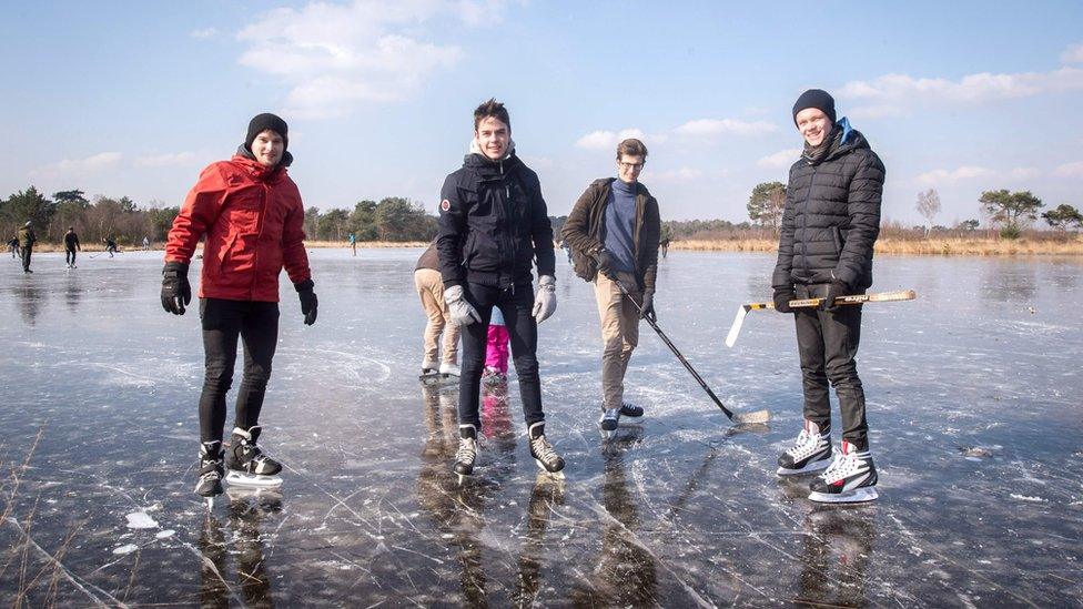 People pose with hockey sticks on a frozen body of water at the Kalmthoutse heide (Kalmthout Heath) nature reserve in Kalmthout on February 28, 2018.