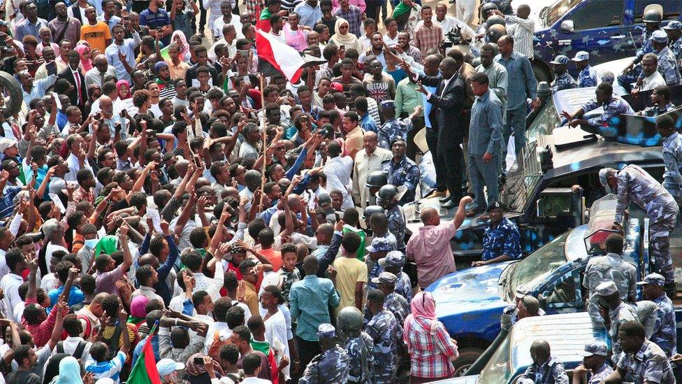 A Sudanese demonstrator waves his hands as he stands on the hood of a security forces' vehicle