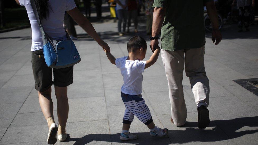 A Chinese couple is seen from the back holding the hands of a child.