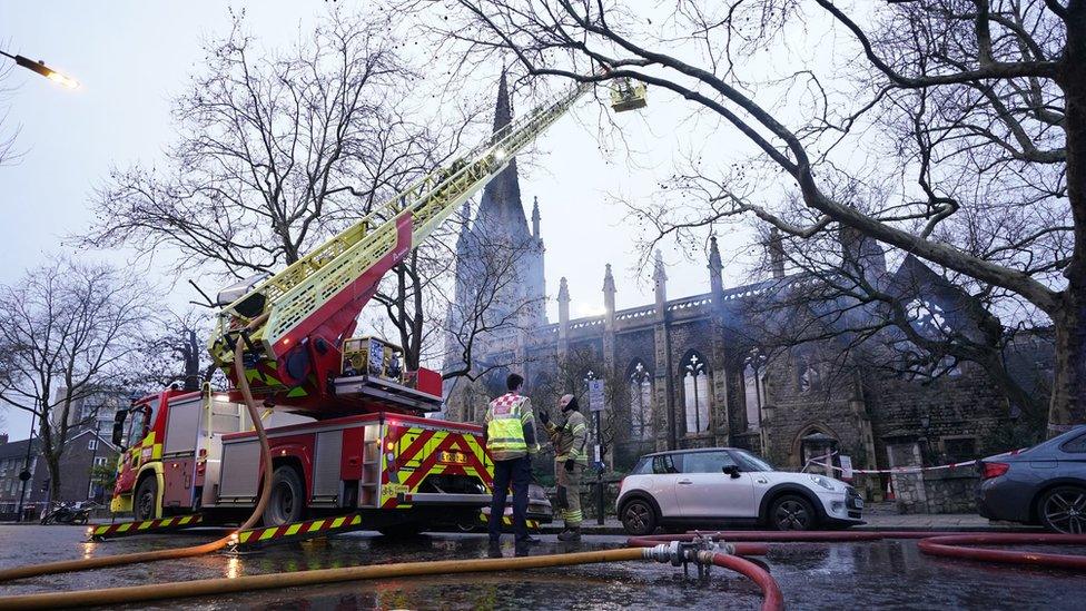 Daytime picture of firefighters using a crane to inspect the collapsed roof of the church.