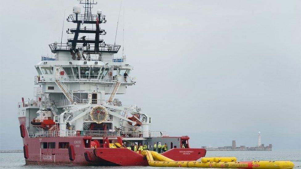 Red and white ship towing a yellow inflatable boom