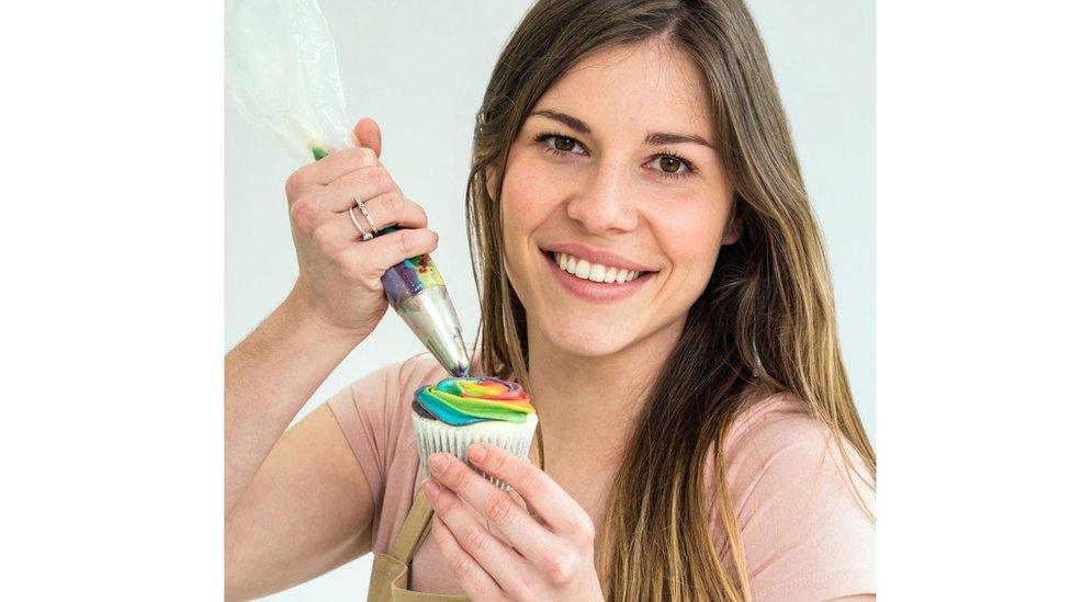 Manon smiles while icing a rainbow cupcake