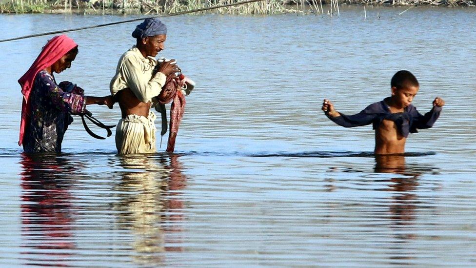 People from Pakistan protect their belongings as they wade through floodwater