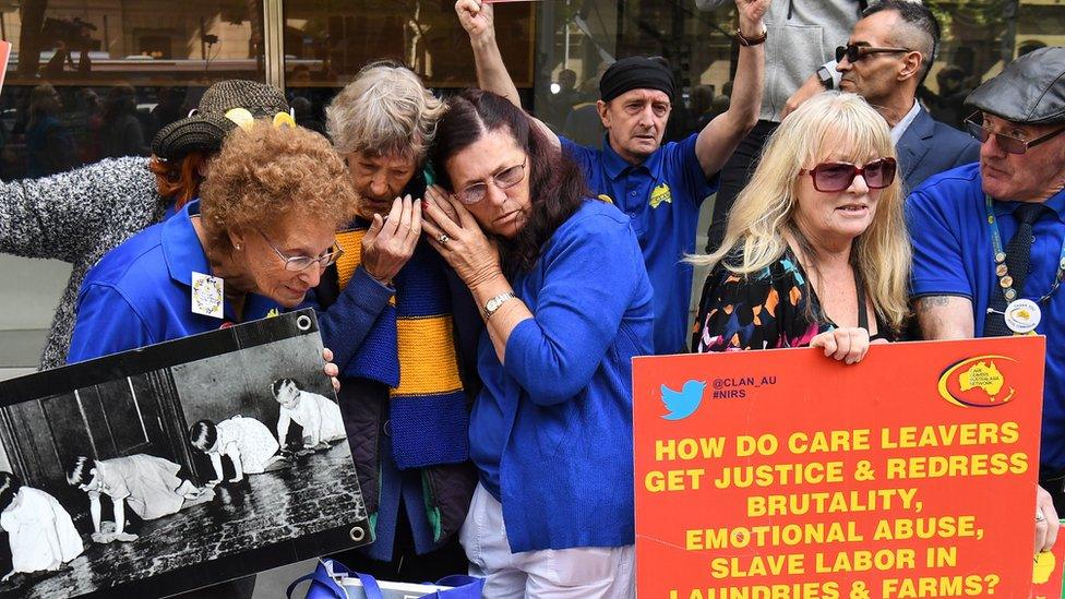 People huddle over a phone to listen to the judge's sentencing remarks while other protesters hold signs outside the court