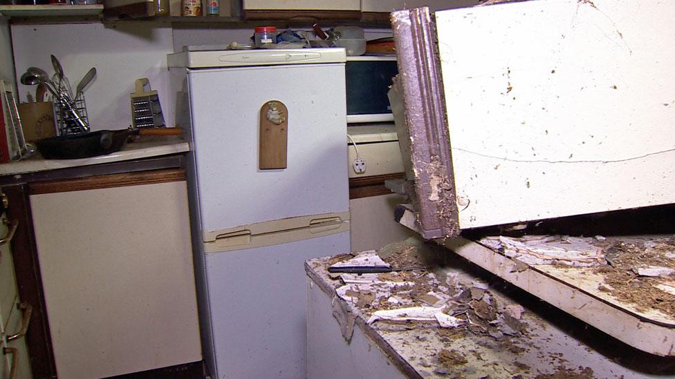 A kitchen where a cupboard seems to have fallen off the wall.